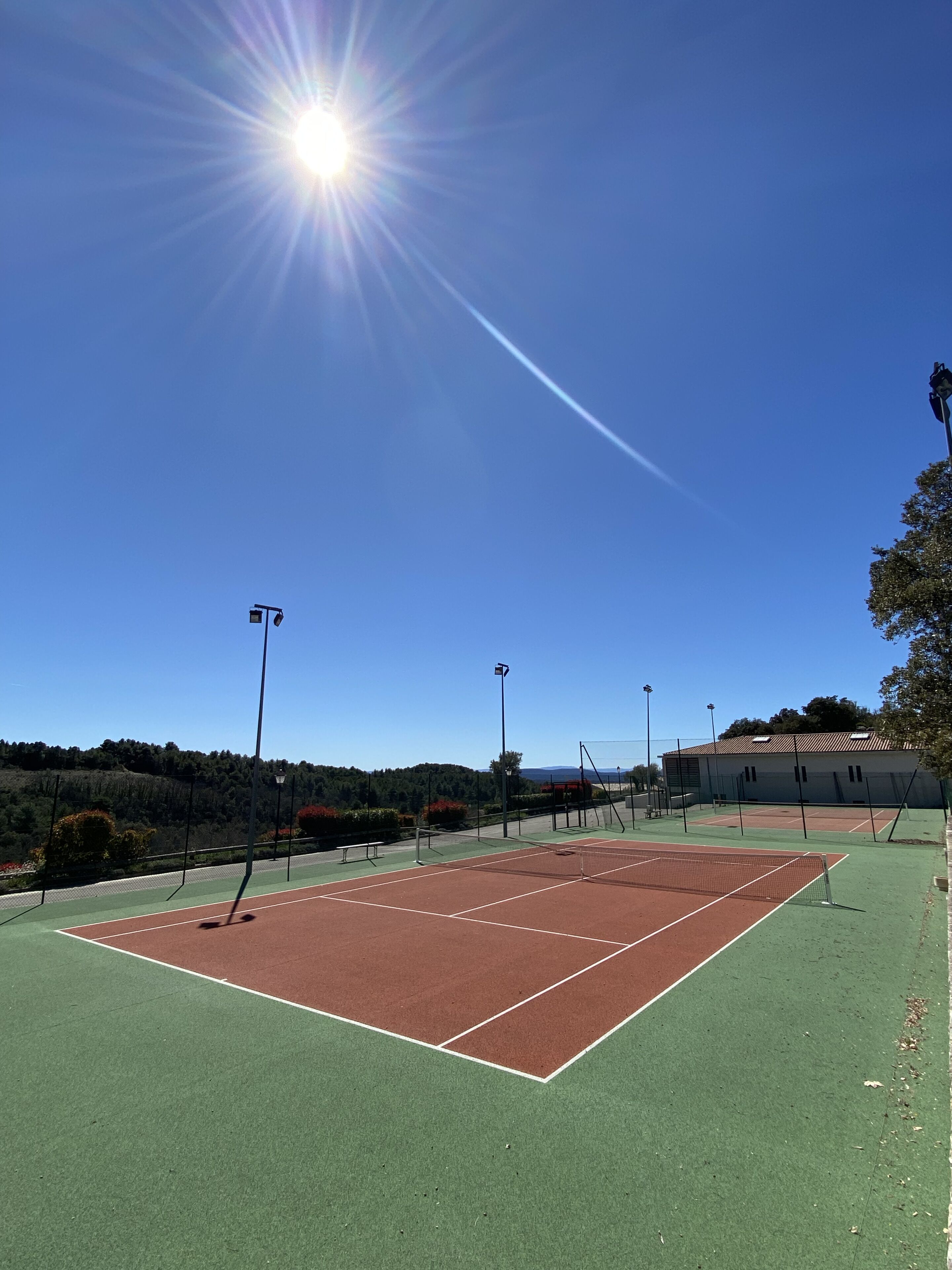 An outdoor tennis court with a clear sky and sunlight.