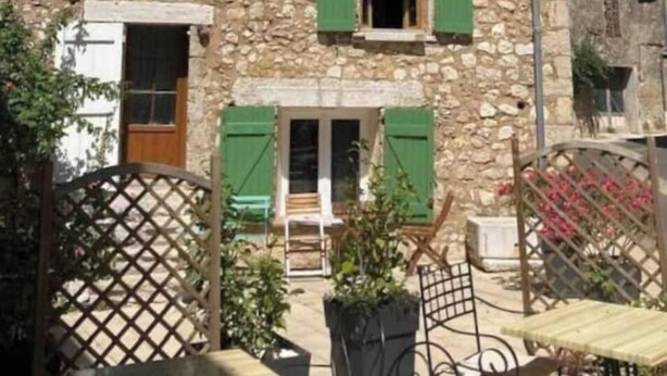 Ein Steinhaus mit grünen Fensterläden, einer Holztür und einem kleinen Balkon.