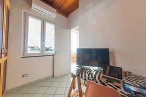 A room with a glass table, a laptop, a TV, and a zebra-patterned cushion.