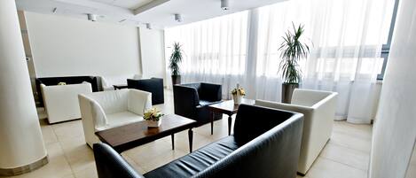 A modern hotel lobby with a seating area, large windows, and potted plants.