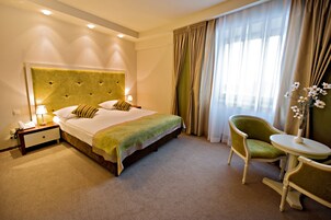 Una habitación de hotel con una cama grande, una mesita de noche con lámpara, una silla y una pequeña mesa.