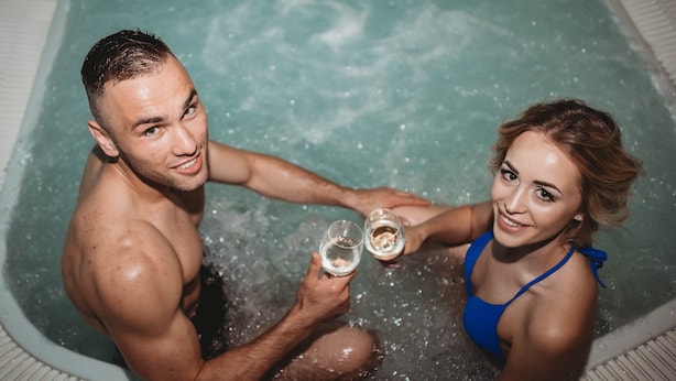 Dos personas en un jacuzzi, sosteniendo copas.