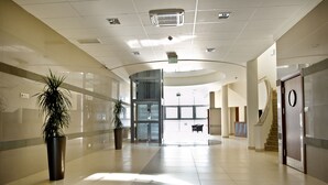 Un hall amplio y moderno con techo curvo, plantas en macetas grandes, una escalera y una zona de recepción.