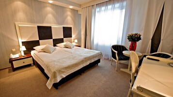 Una habitación de hotel con una cama grande, un escritorio, una silla y una mesita de noche con lámpara.