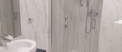 Un baño con ducha de vidrio, lavamanos con encimera de mármol y un inodoro.