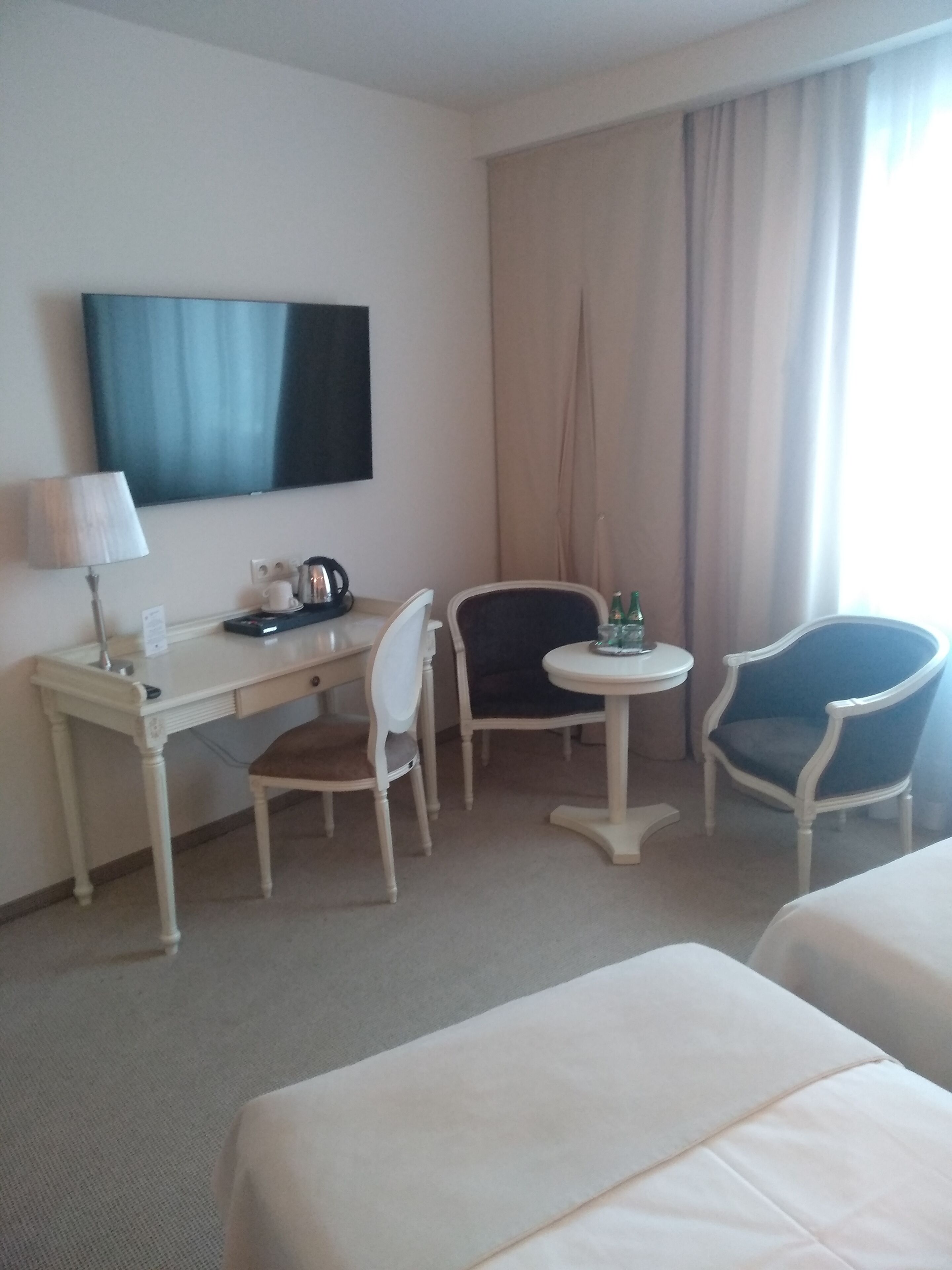 A hotel room with a desk, two chairs, a television, and two beds.