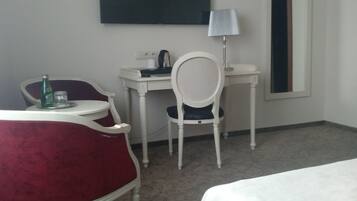 A hotel room with a bed, a desk, a chair, a lamp, and a television on the wall.