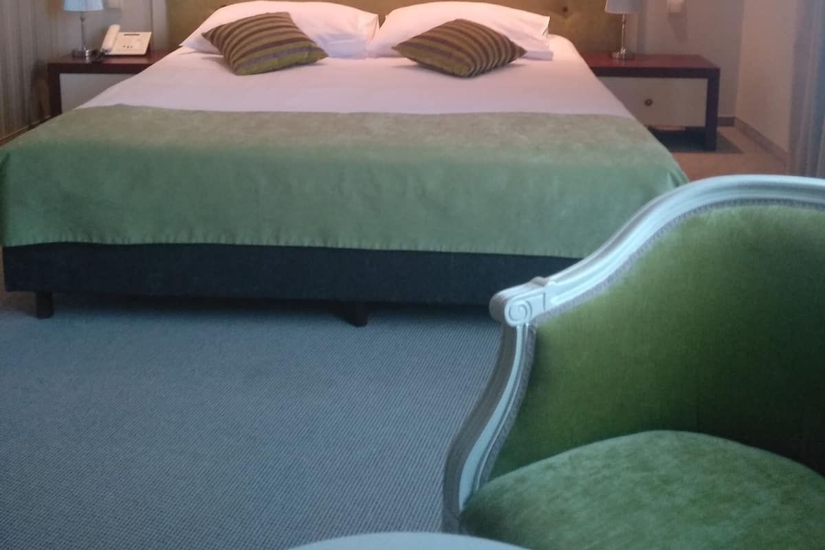 A hotel room with a large bed, two bedside tables with lamps, a green armchair, and a small round table.