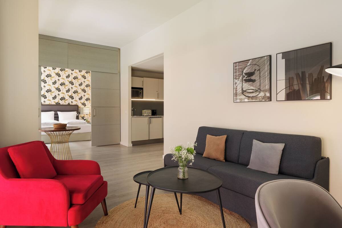 A modern living room with a red armchair, grey sofa, and a small coffee table with a vase.
