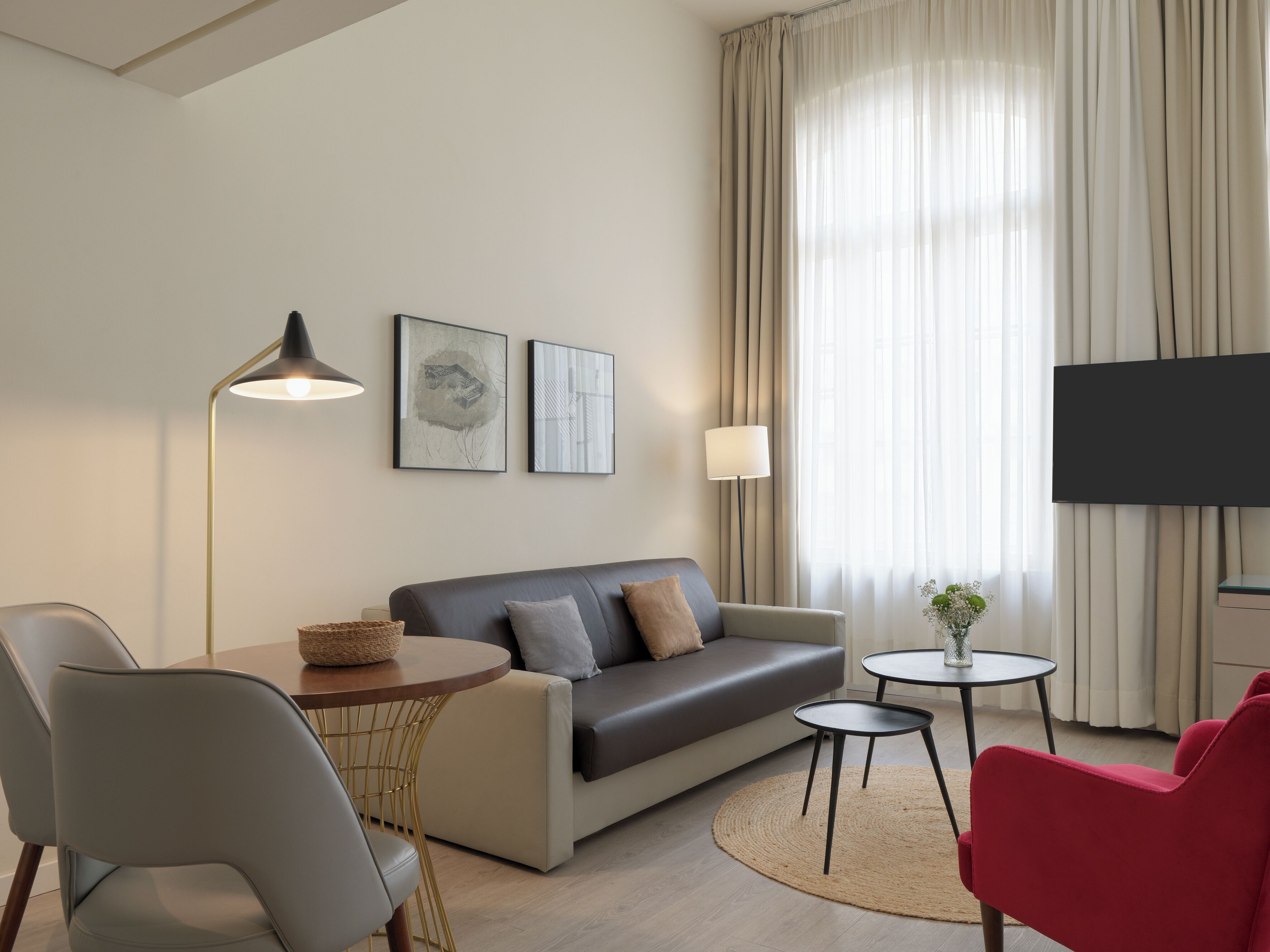 A modern living room with a sofa, a round table, a red chair, a floor lamp, and a flat-screen TV.