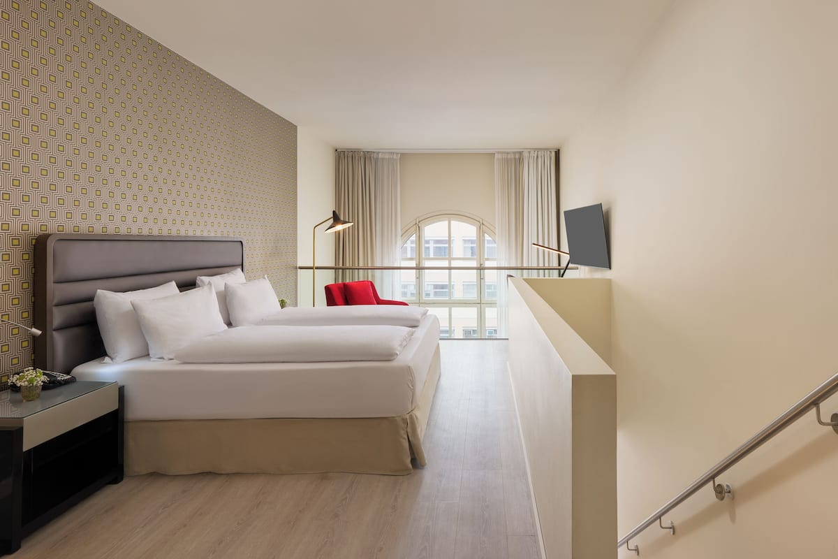A modern hotel room with a bed, bedside table, lamp, and a TV on the wall.