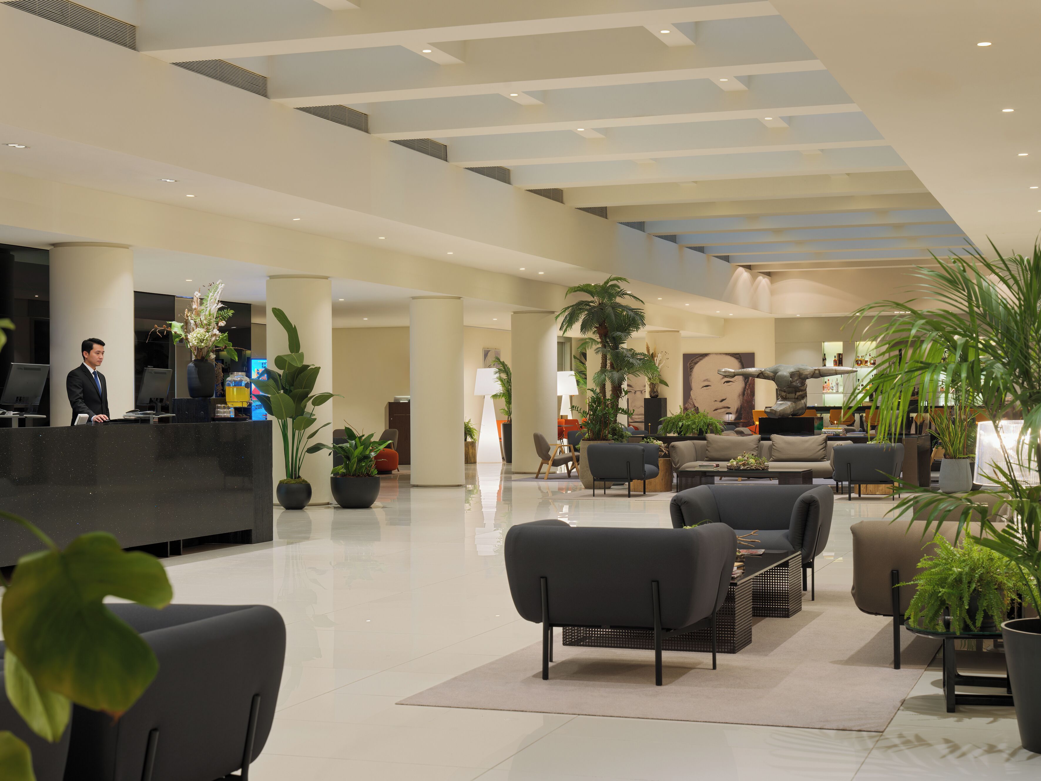 A modern hotel lobby with a reception desk, seating area, and potted plants.