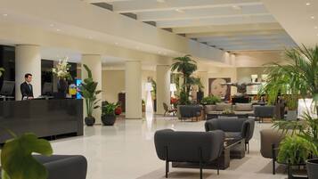 Un moderno vestíbulo de hotel con mostrador de recepción, zona de estar y plantas en macetas.