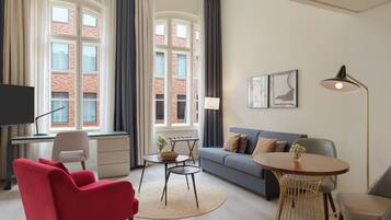 Een moderne woonkamer met een rode fauteuil, een grijze bank, een ronde tafel en een televisie op een bureau.