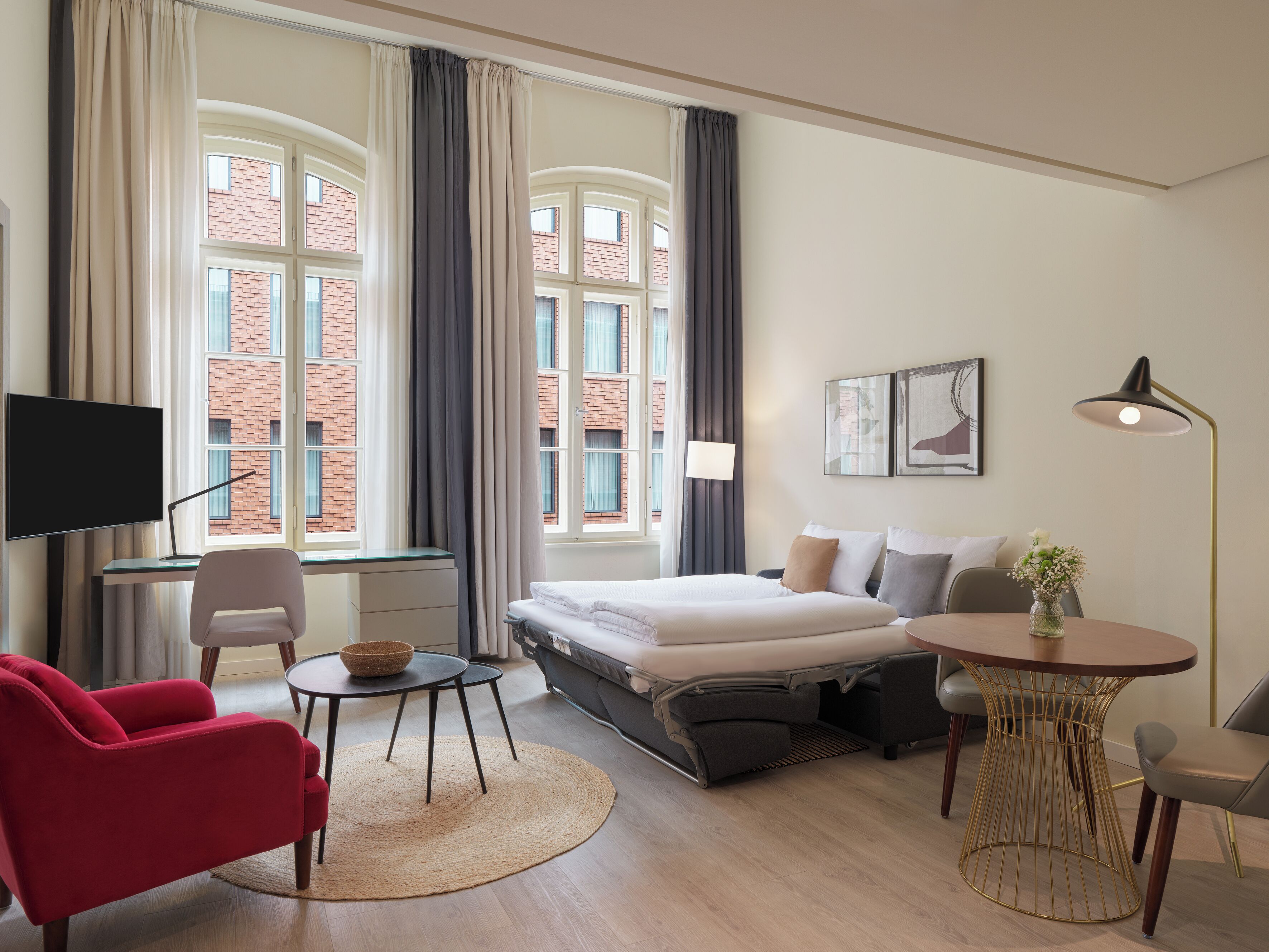 A modern hotel room with a bed, desk, chair, and a small table with a bowl.
