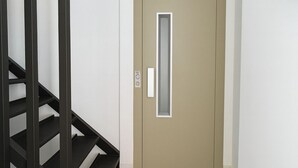 Un couloir avec une porte beige, un escalier noir et un extincteur fixé au mur.