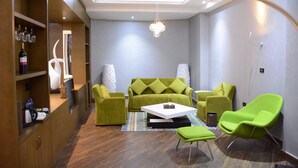 Ein modernes Wohnzimmer mit einem grünen Sofa, zwei grünen Sesseln, einem weißen Couchtisch und einem gemusterten Teppich.