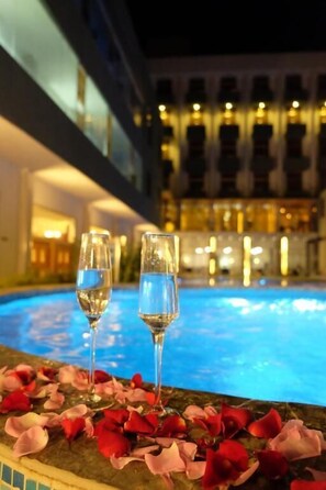 Vista da piscina com dois copos de água e pétalas de rosa na borda.