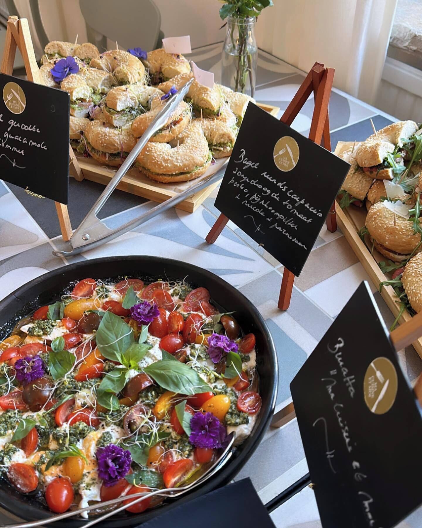 A buffet table with various dishes, including a salad with tomatoes and greens, and several types of sandwiches.