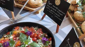 A buffet table with various dishes, including a salad with tomatoes and greens, and several types of sandwiches.