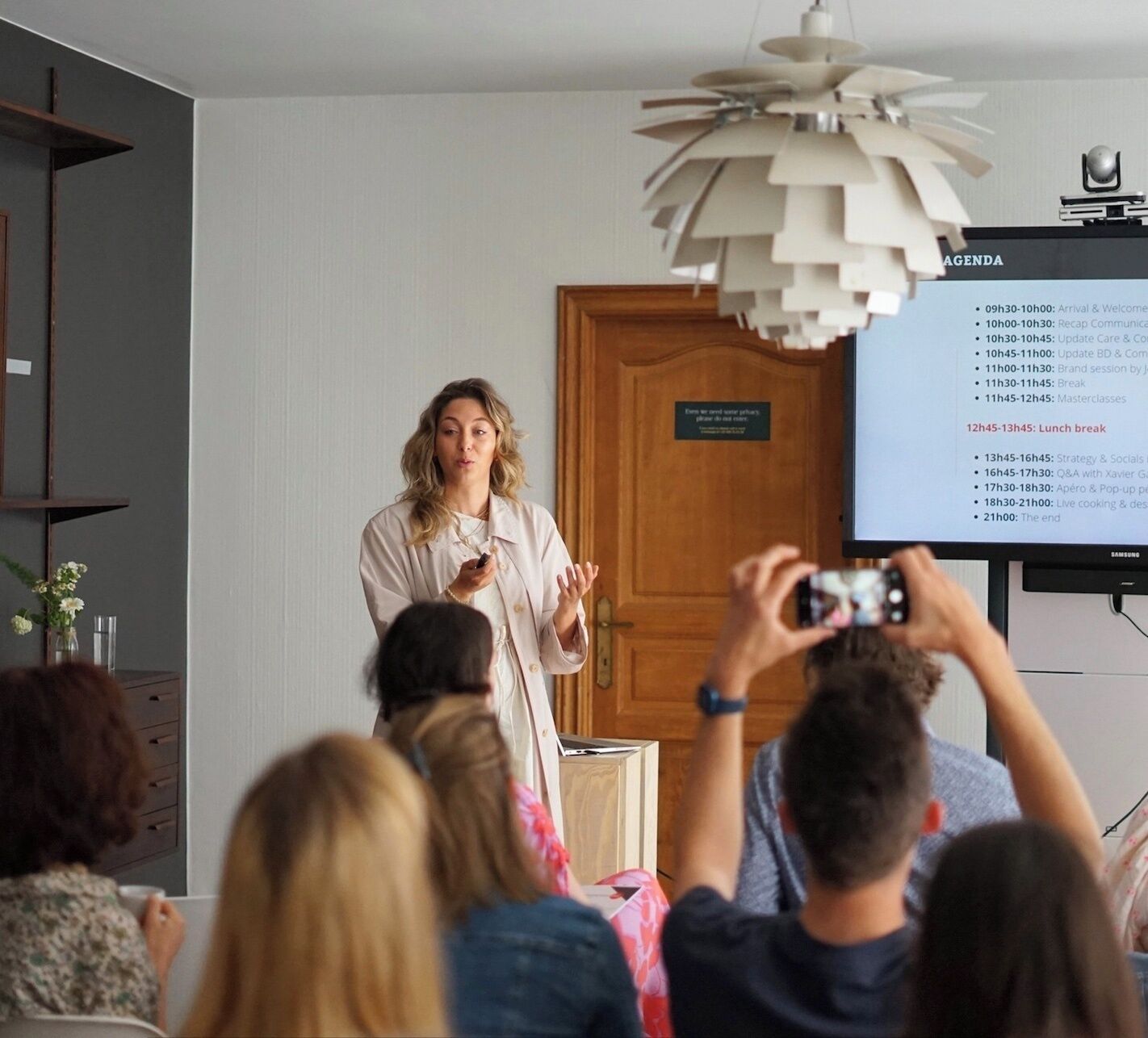 A person presenting in a room with a projector displaying an agenda.