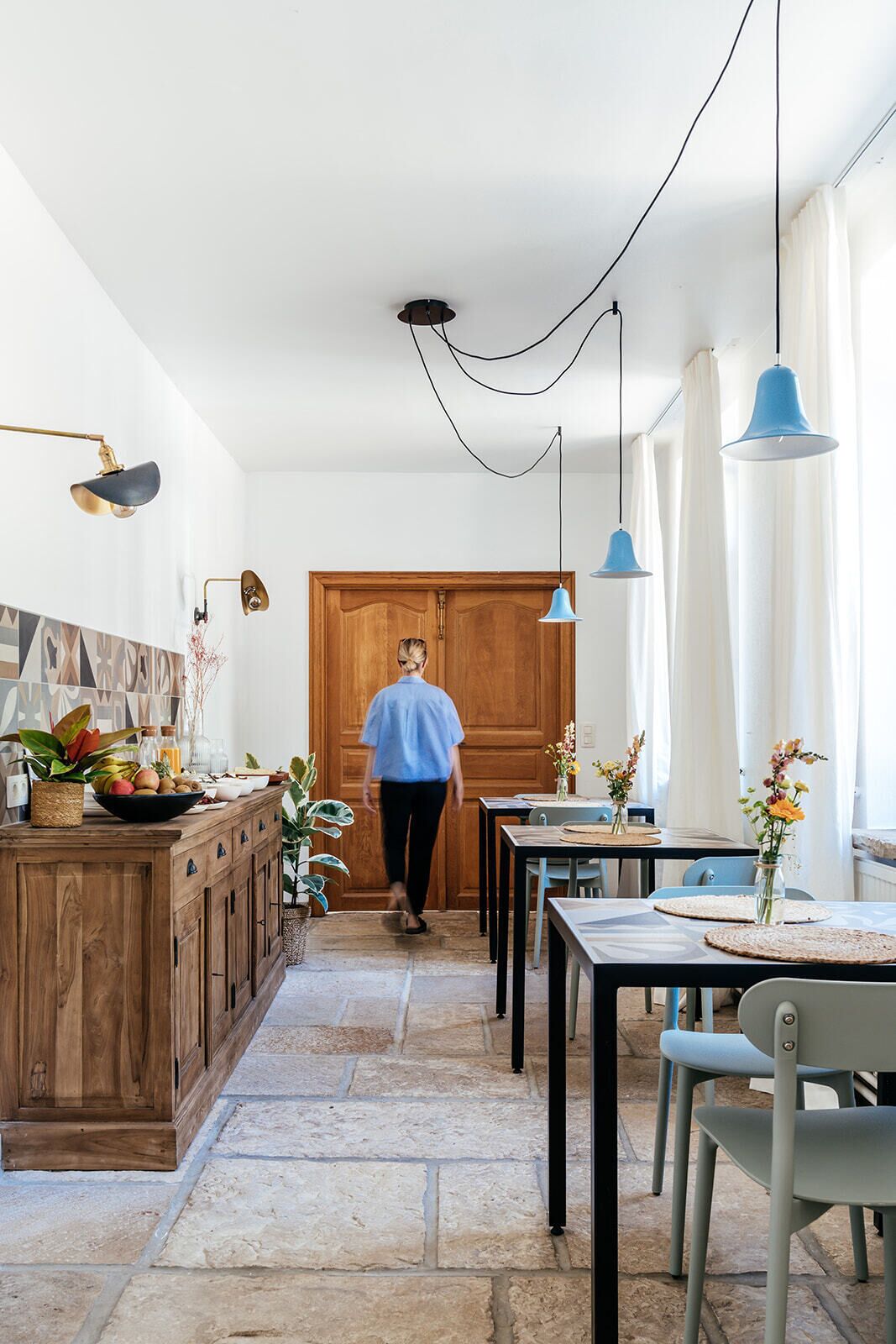 A kitchen with a wooden cabinet, a dining table with chairs, and hanging pendant lights.