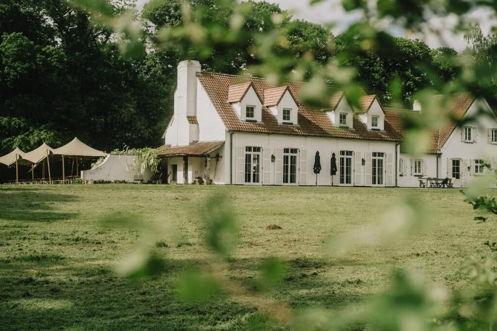 A large white building with a tiled roof, surrounded by a grassy field and trees.