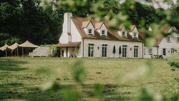 A large white building with a tiled roof, surrounded by a grassy field and trees.