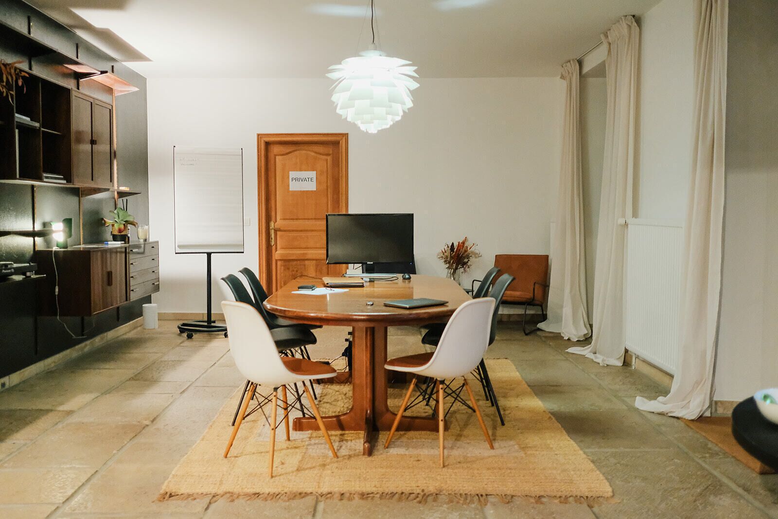 Een moderne eethoek met een ronde houten tafel, vier stoelen, een televisie en een decoratieve hanglamp.