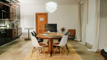 Een moderne eethoek met een ronde houten tafel, vier stoelen, een televisie en een decoratieve hanglamp.