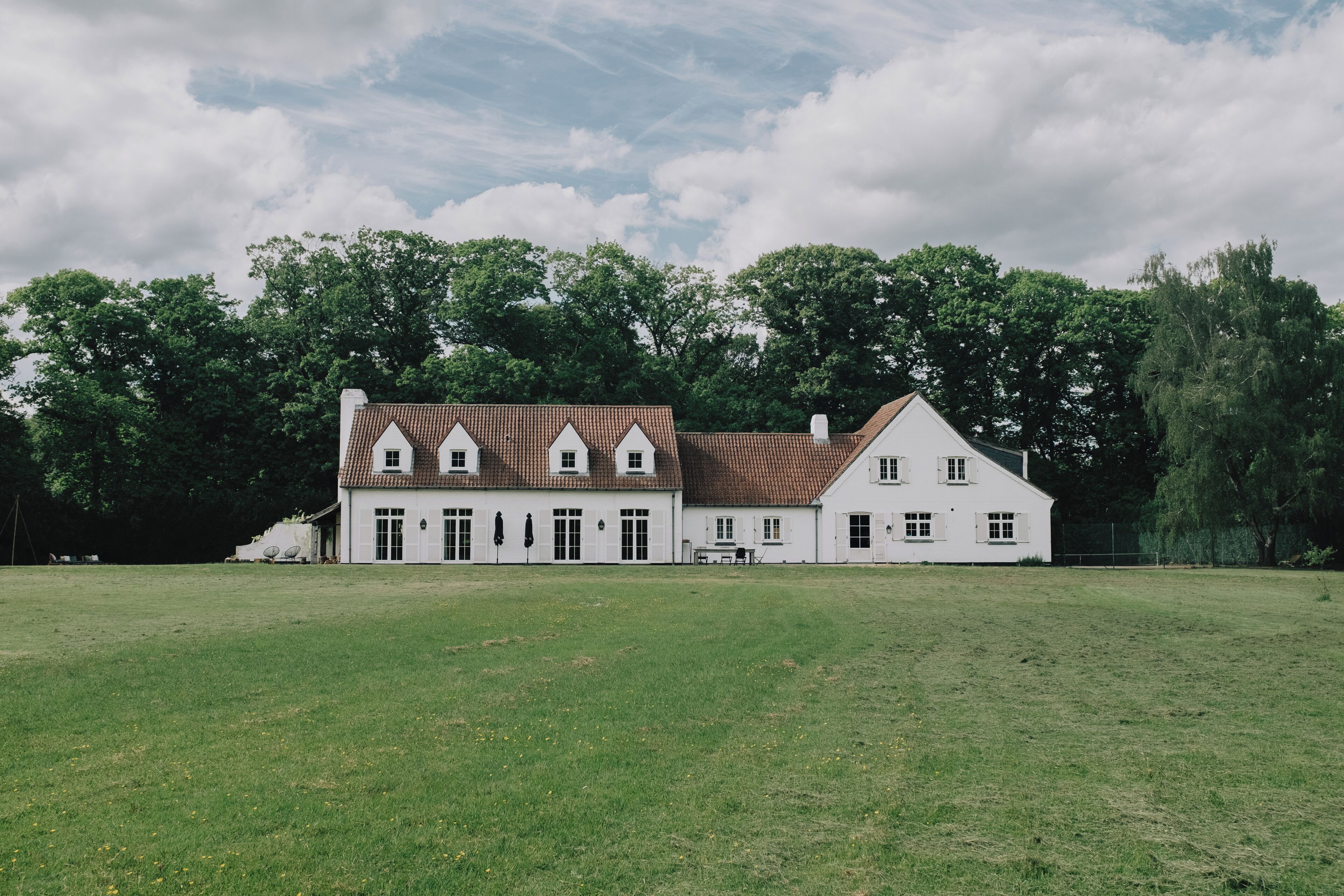 A large, white building with a tiled roof and multiple windows, surrounded by a grassy field and trees.