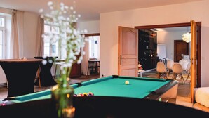 A pool table with balls, a candle, and a vase of flowers in the foreground. There is a dining area with chairs and a table in the background. - Villa Parkbos (De Pinte)