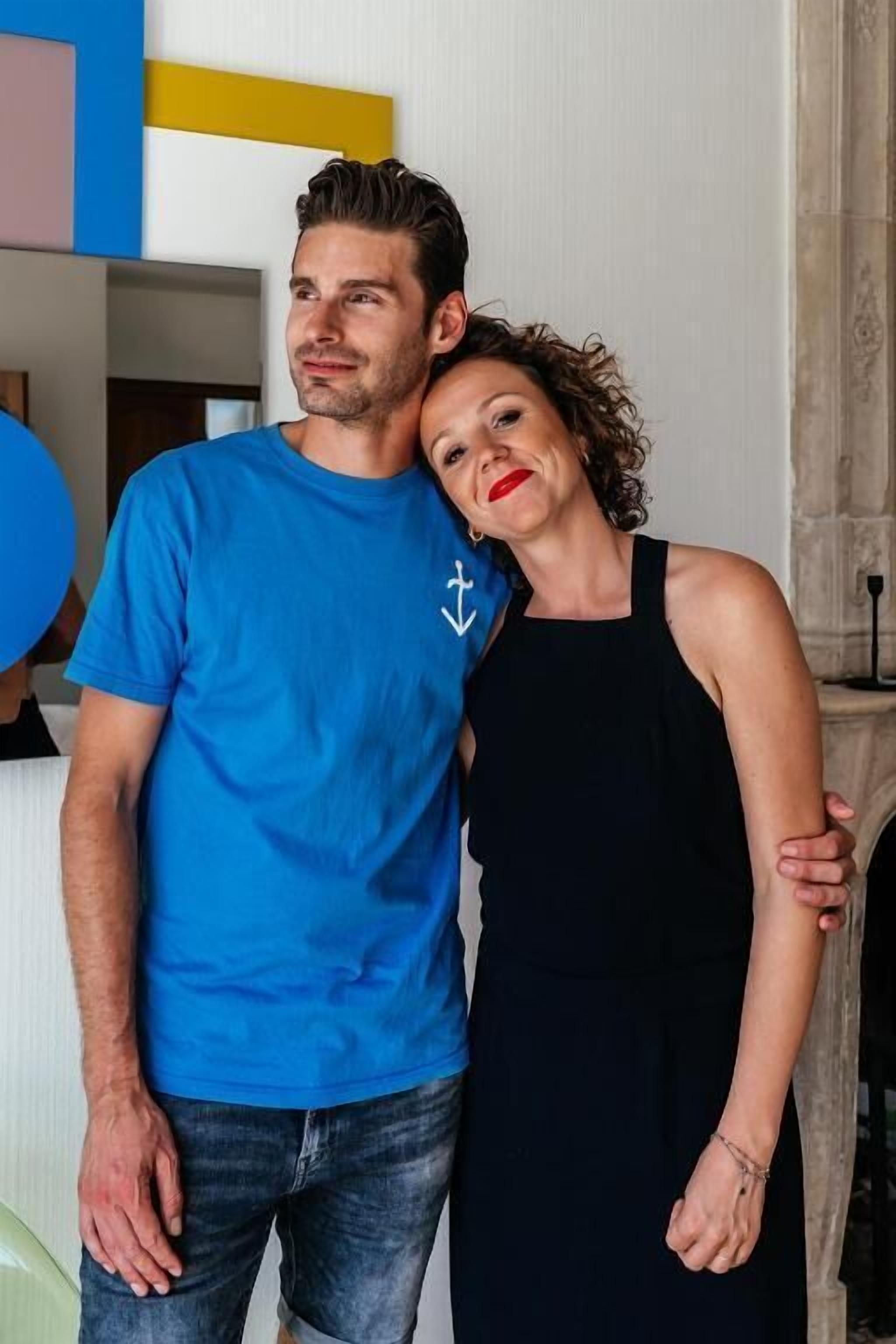 A man and a woman standing close together in a room with a modern interior design, including a fireplace and a decorative wall.