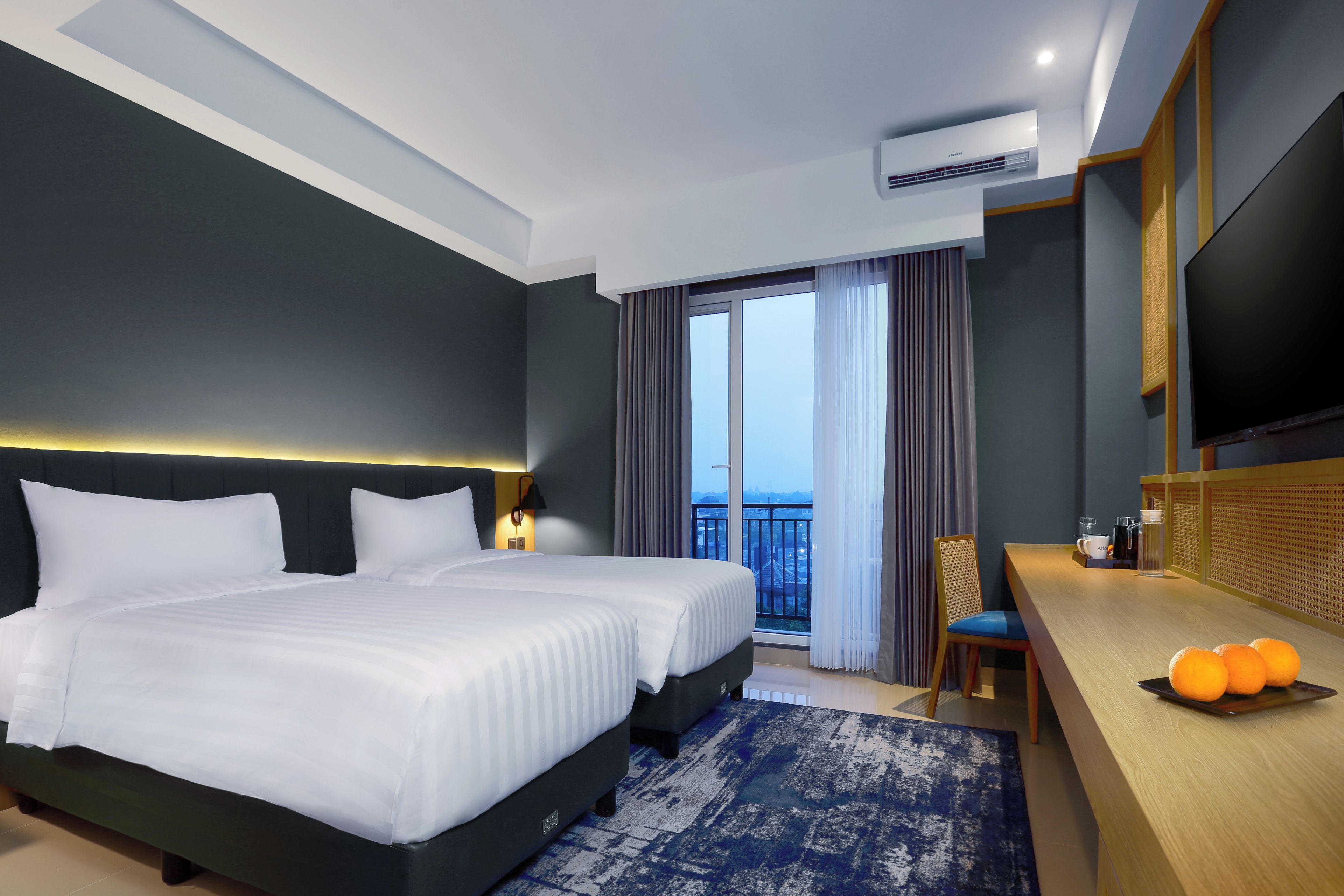 Une chambre d’hôtel moderne dotée d’un grand lit, d’un bureau avec une chaise, d’une télévision à écran plat et d’un balcon avec des rideaux.