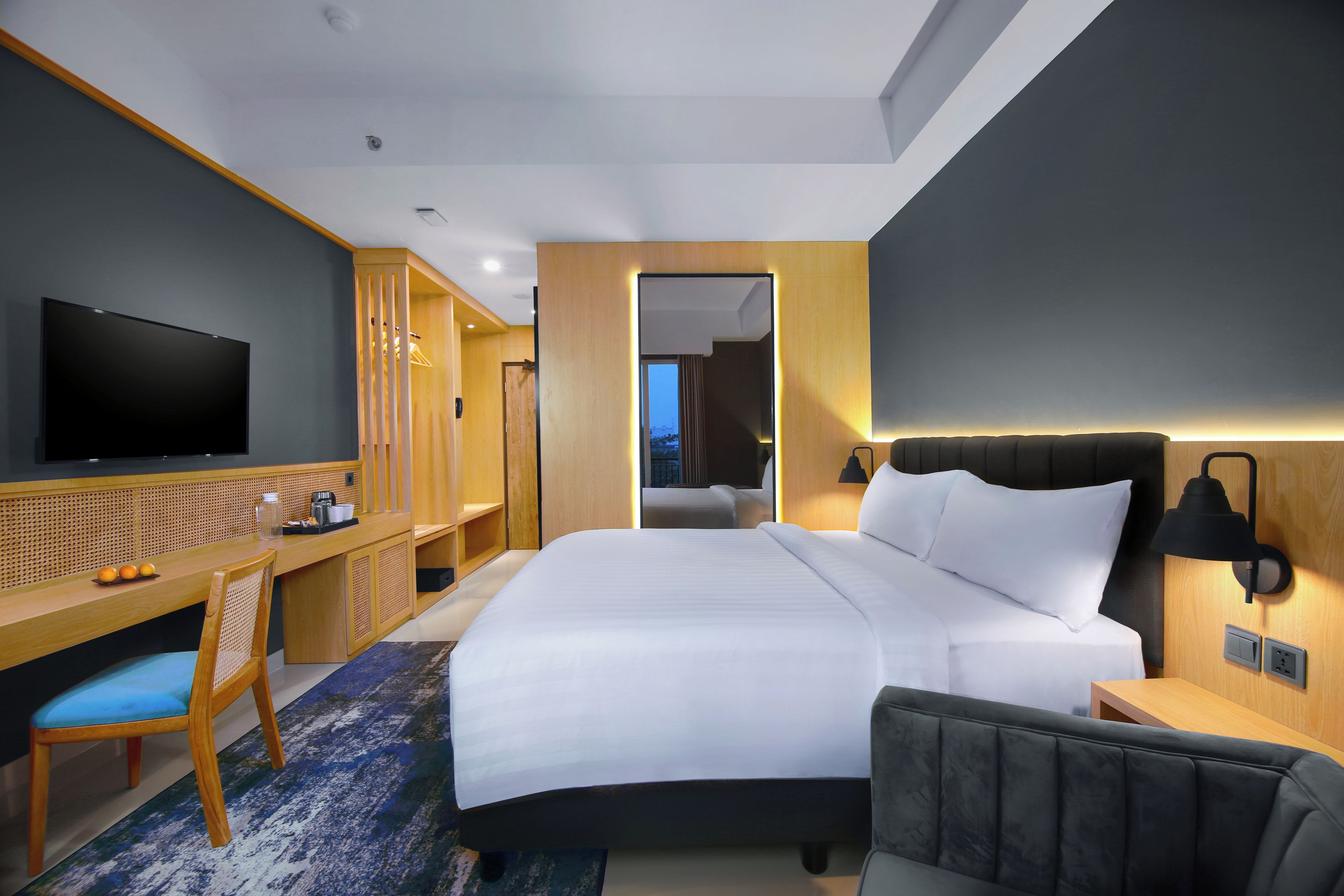 Habitación de hotel moderna con una cama grande, un escritorio con televisor de pantalla plana, zona de estar y vistas a la ciudad al atardecer.