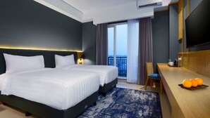 Et moderne hotelværelse med en stor seng, et skrivebord med appelsiner og udsigt over byen fra vinduet.
