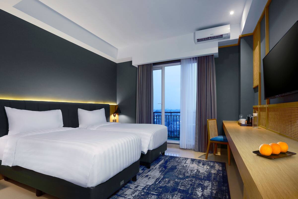Een moderne hotelkamer met een groot bed, een bureau met sinaasappels en uitzicht op de stad door het raam.