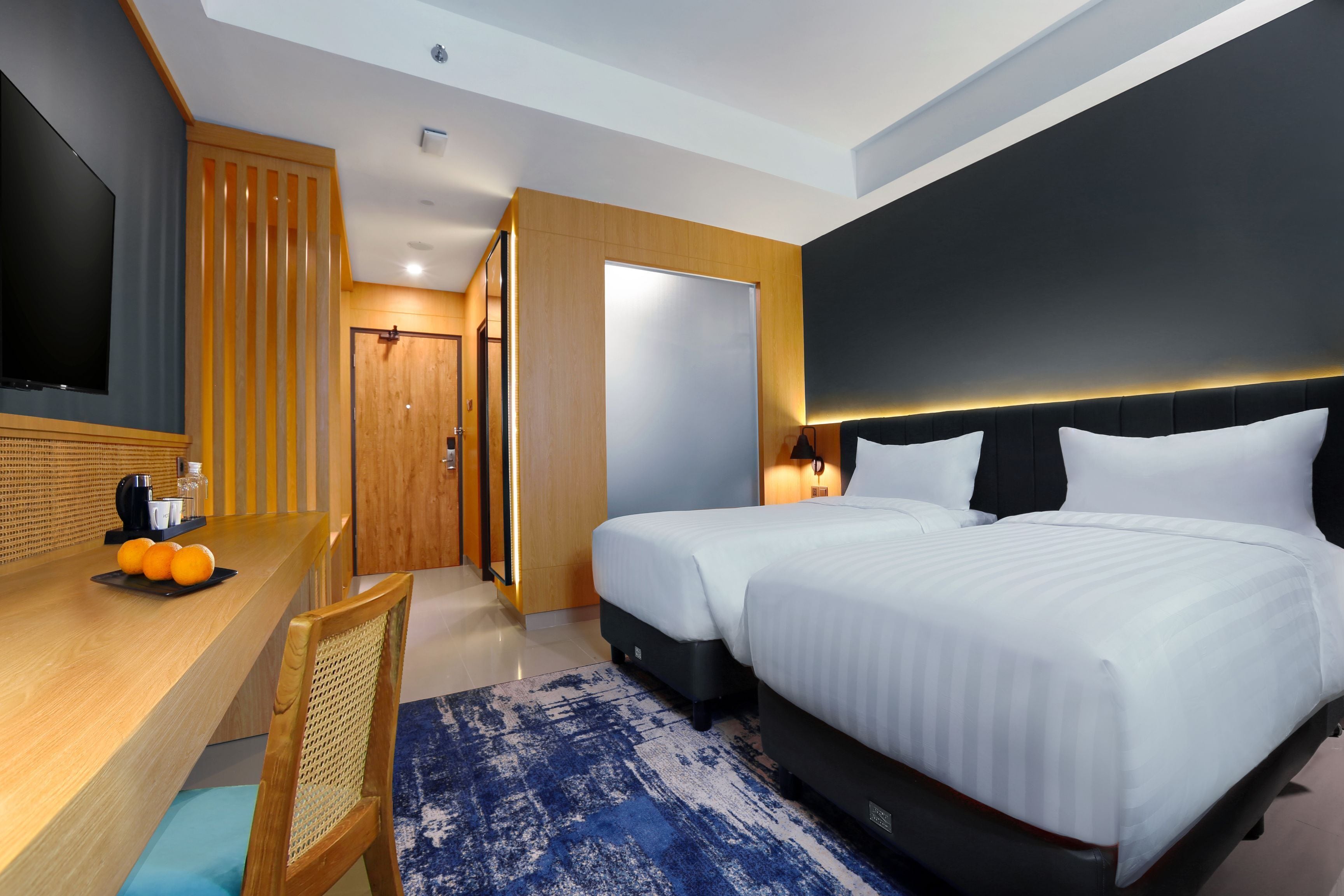 A hotel room with two beds, a desk with a chair, a TV, and a bathroom door.
