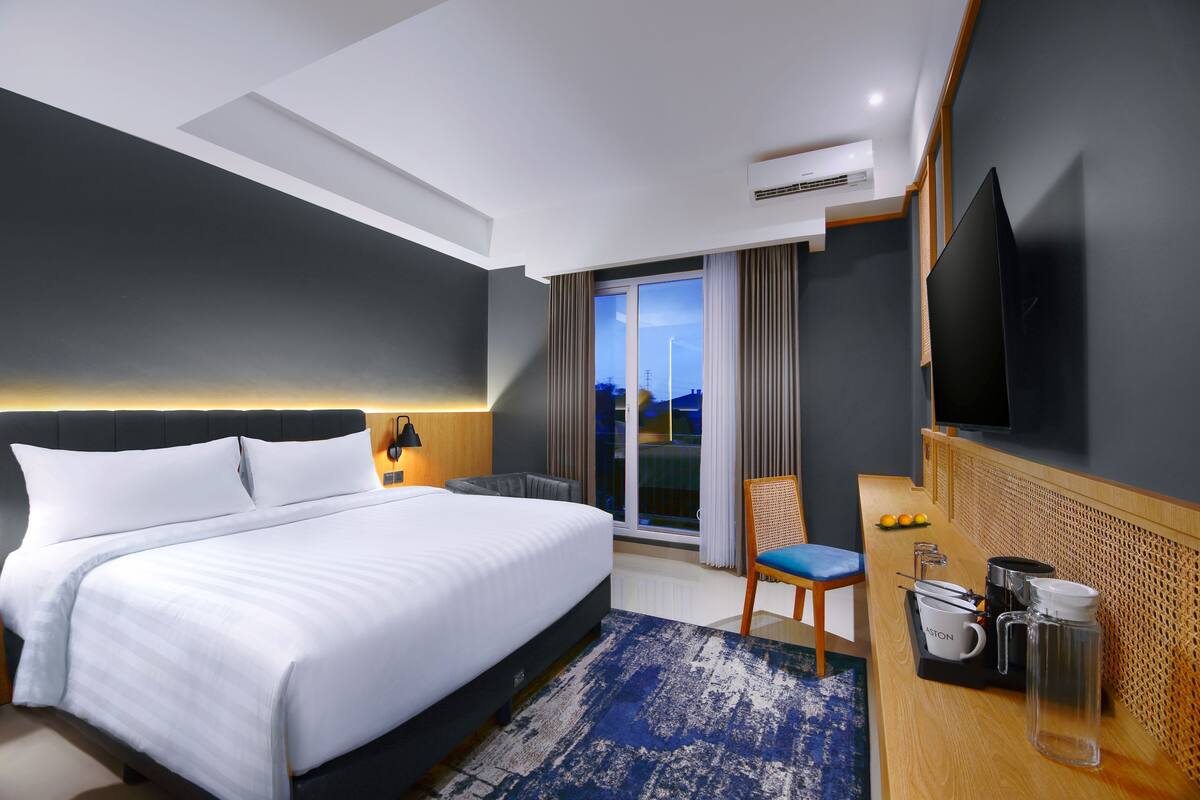 Een moderne hotelkamer met een groot bed, een bureau met stoel, een flatscreen televisie en uitzicht op de skyline.