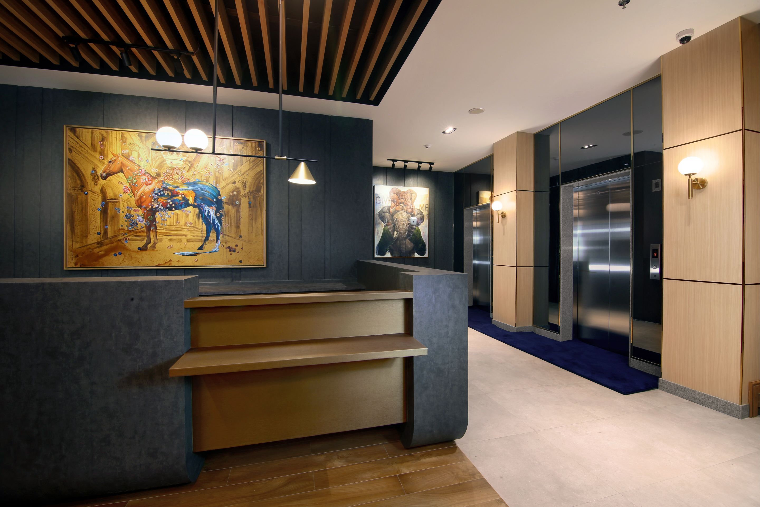 A modern reception area with a wooden reception desk, a large painting, and a sleek elevator.