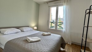 Une chambre à coucher avec un lit, une fenêtre avec des rideaux, un radiateur et une échelle en métal noir.