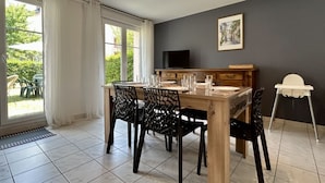 Un espace repas comprenant une table, des chaises, un téléviseur et une chaise haute blanche.