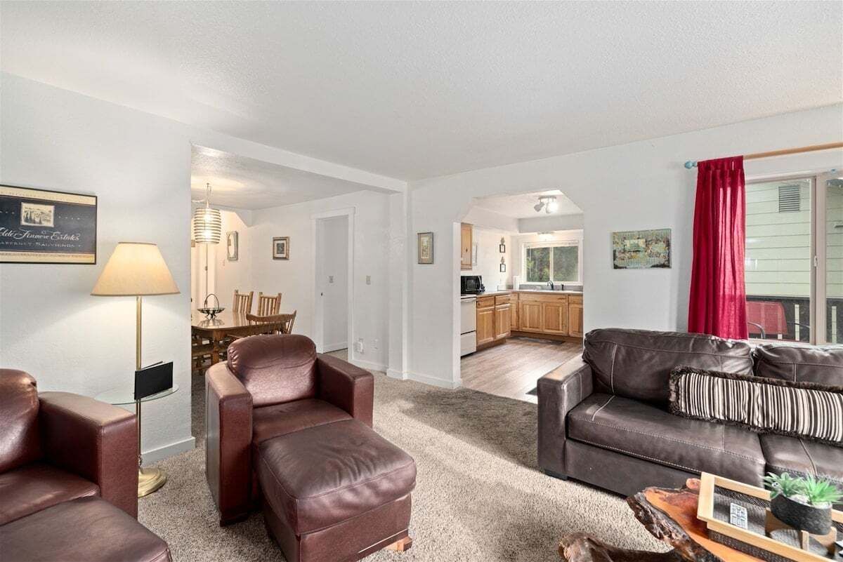Ein Wohnzimmer mit braunem Ledersofa, einem roten Vorhang und einem Essbereich mit Tisch und Stühlen.