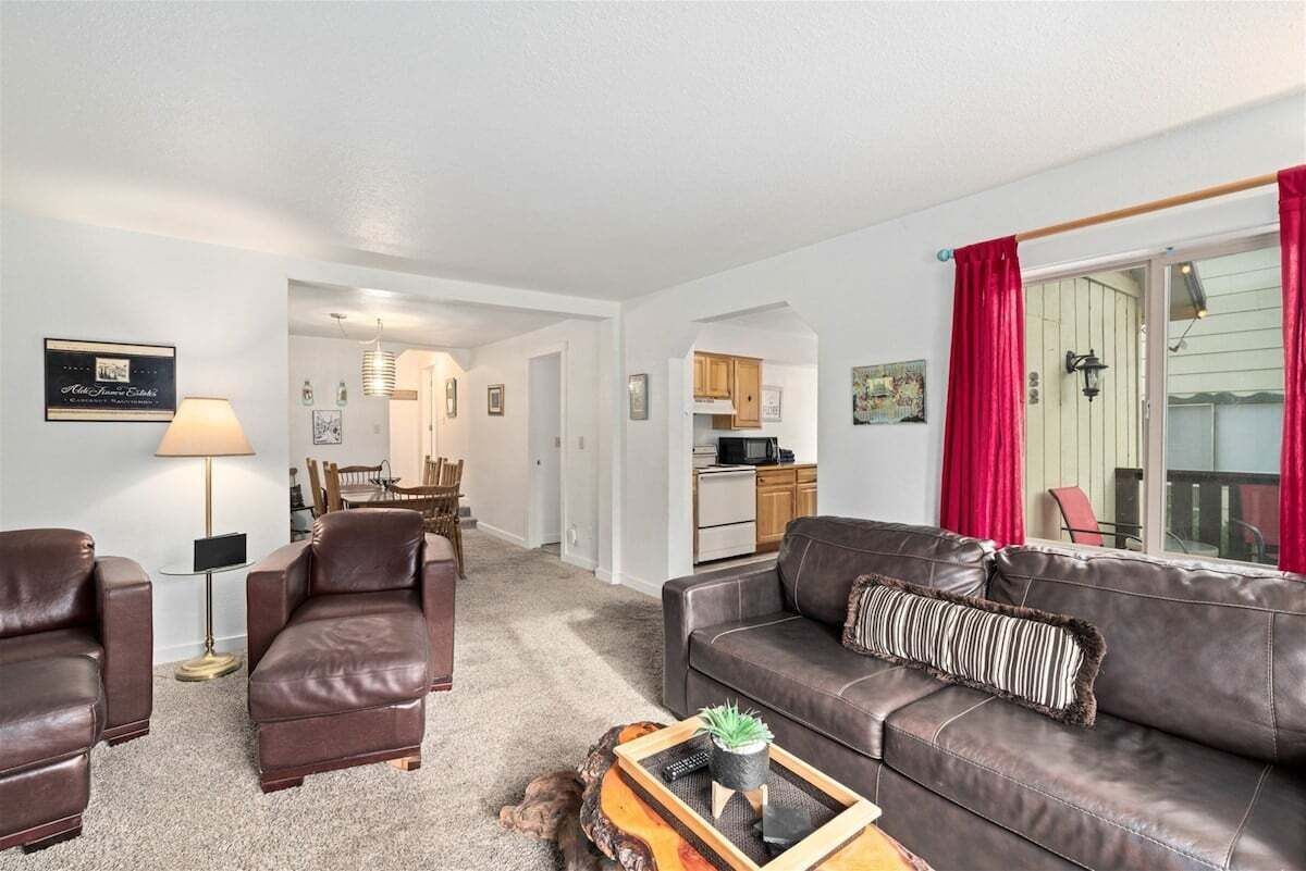 Ein Wohnzimmer mit einer Couch, Sesseln, einem Couchtisch und einer Küche im Hintergrund.