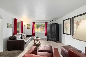 A living room with a sofa, ottoman, cabinet, and artwork on the walls. - Bavarian Suites, #22 -In the Heart of Town (Leavenworth)