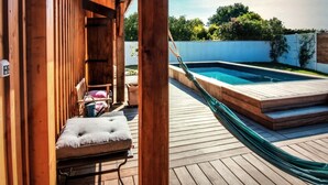 Une terrasse en bois avec un hamac, une petite piscine et un coin salon agrémenté de coussins.