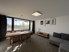 A modern living room with a dining area, large windows, and artwork on the walls.