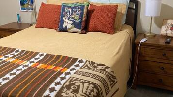 Restful retreat with a neatly made bed, a framed mountain landscape, and a bedside table with a lamp and drawer.