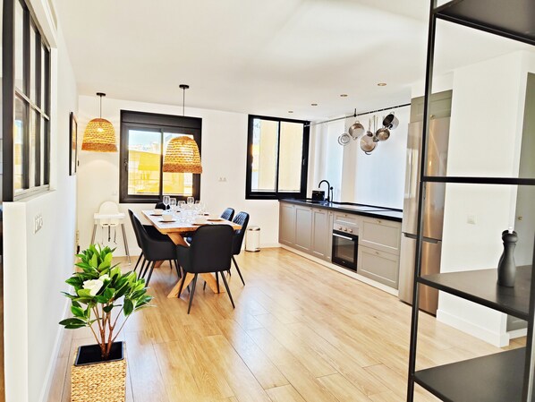 A modern kitchen with a dining area, featuring a wooden table, black chairs, and a hanging pot rack.