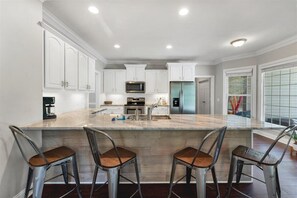 A modern kitchen with a large island, stainless steel appliances, and white cabinetry. - This is it! | Pool | Golf | Convenient to Town (Southern Pines)